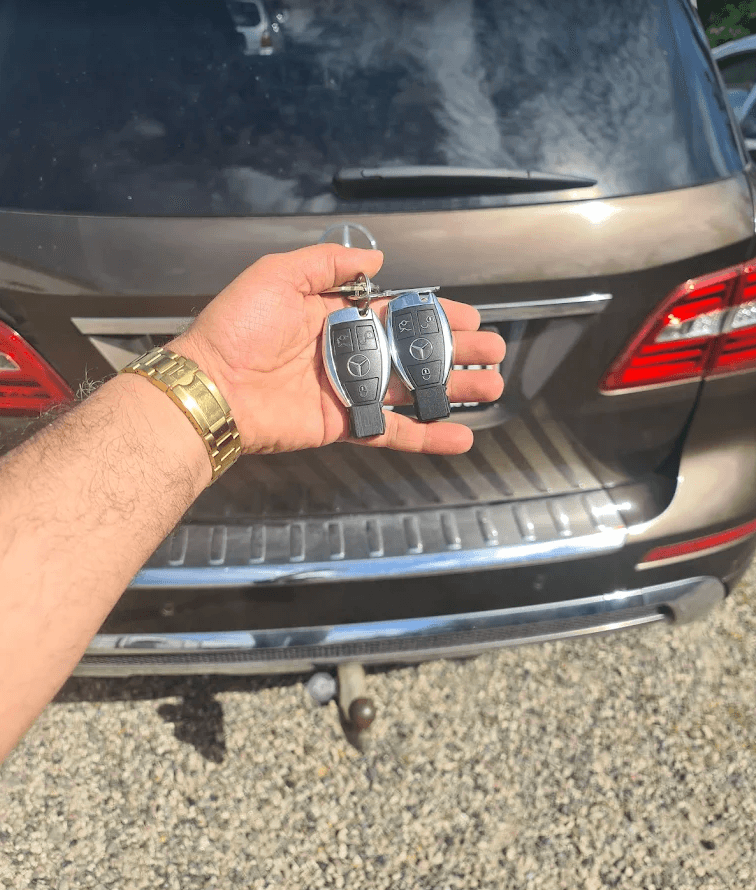 Hånd holder to nyprogrammerede Mercedes-Benz smartkeys foran bilen.